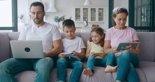 4K video of family members focused on work on personal digital device. Young father freelancer working on laptop, mother on digital tablet and cute children sitting between their busy parents