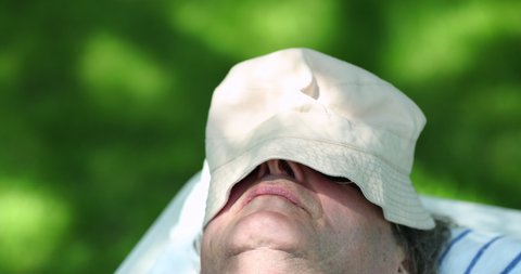 Older man asleep outside covered by hat under tree, close-up senior person face napping during siesta