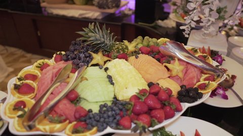 Assorted fruits on the buffet table. Fresh ripe exotic fruits in a plate. Sliced melon, watermelon, pineapple and orange, strawberries, blueberries and blackberries and grape twigs