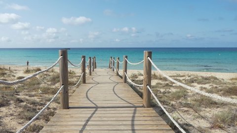 Wooden path giving access to a golden sandy beach with clear water in Southern Europe - Minorca.