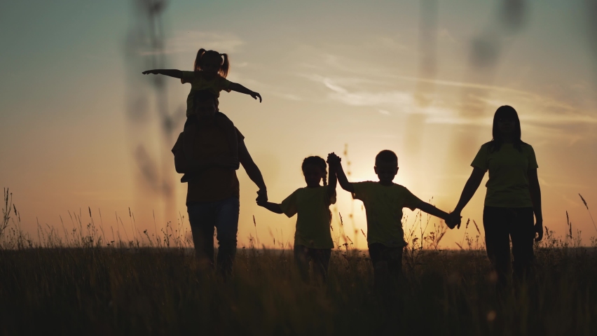 Happy family at sunset. Silhouette of group of people walk in park. Happy child with parents holding hand. Family is walk in park on grass. Happy family concept. Parents hold hand of their child. Royalty-Free Stock Footage #1077869279