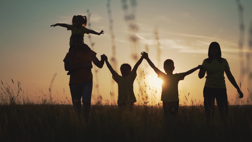 Happy family at sunset. Silhouette of group of people walk in park. Happy child with parents holding hand. Family is walk in park on grass. Happy family concept. Parents hold hand of their child. | Shutterstock HD Video #1077869279