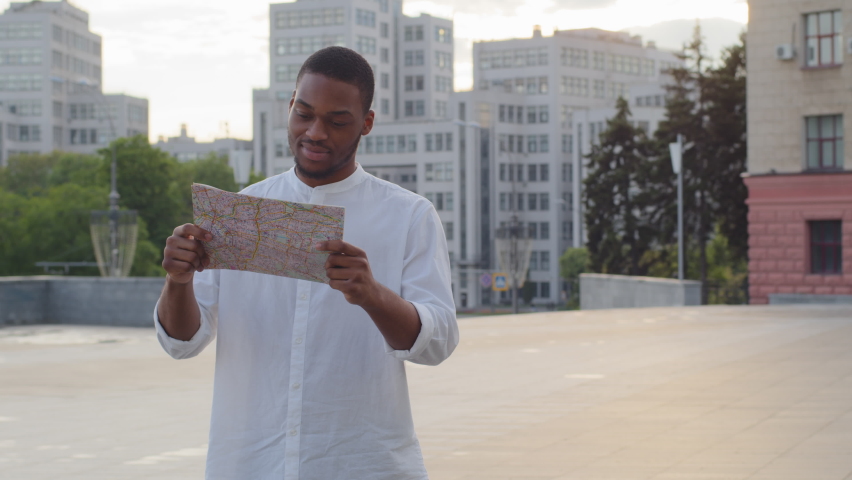 Afro american young guy african millennial business man male tourist traveler foreign student standing outdoors in new city on street looking around and in map searching for location route road lost