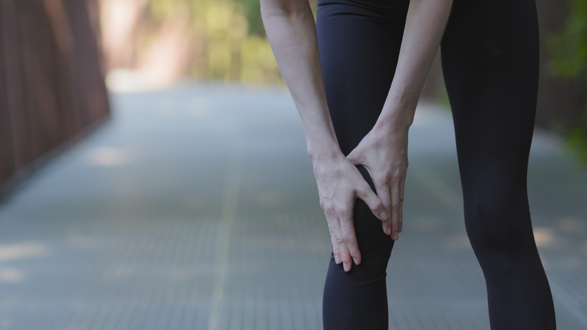 Close-up female legs in black leggings of unrecognizable slender active strong woman runner jogging running morning run training stops feeling knee pain ache suffers from damage joint problems injury | Shutterstock HD Video #1077869783