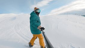 Man riding on snowboard with selfie stick in his hand downhill snowy mountain. Guy filming himself during riding down. Concept of extreme, sport, winter, freeride, snowboarding
