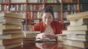 Asian woman watching video on phone at library, laughing, disturbing others