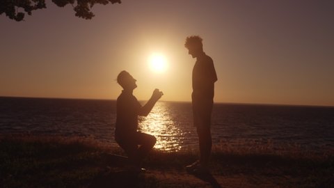 Silhouette of gay man kneeling to propose to boyfriend, romantic engagement