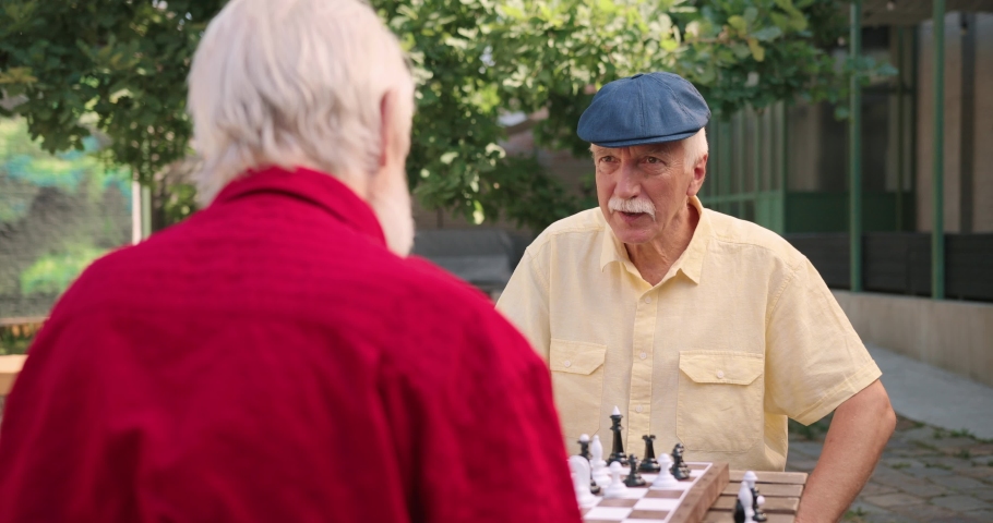 Waist up portrait view of the caucasian old retired and smiled man moving a chessman on the board and smiling toothy. Outside. Leisure games concept