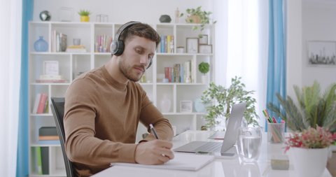 Focused happy caucasian young man having video conference call at home office. Millennial man using headphones working or studying from home. Online learning or teleworking.