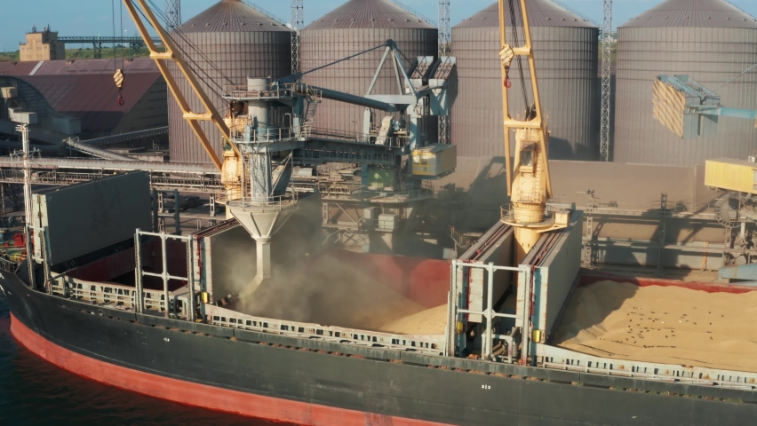 Drone video - loading grain into holds of sea cargo vessel through an automatic line in seaport from silos of grain storage. Bunkering of dry cargo ship with grain Royalty-Free Stock Footage #1077875585