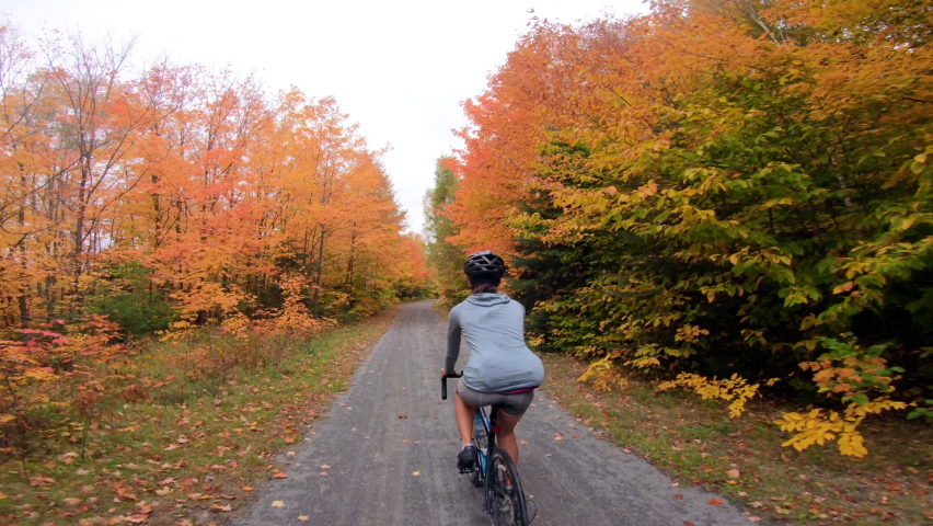 Road gravel biking in Fall on forest path with colorful orange yellow autum leaves. Road biker riding bicycle in fall foliage. Woman living healthy sports lifestyle outdoors.