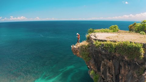 Aerial view active lifestyle people standing on top mountain cliff on background sand beach and azure clear ocean at sunny day. Active lifestyle and Travel concept. 4K Aerial UHD Video Clip. 