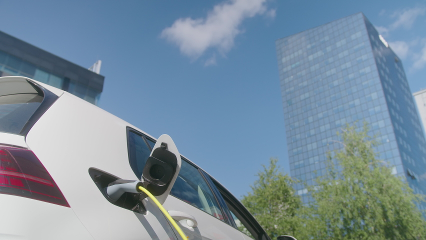 Handheld shot of a smiling Caucasian young woman unplugging the electric car charger at a downtown charging point