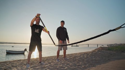 An athlete on the beach, trains simulates rowing on a surfboard and receives instructions from a personal fitness trainer. Preparing for competitions. Portugal Faro 2021 March 15 