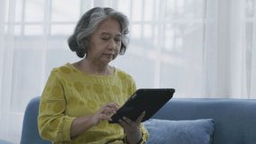 Asian elderly woman video calling and talking, smiling, happy family In living room. Stay at home. Telehealth consult doctor with tablet. Senior practice social play with tablet. Concept Telemedicine