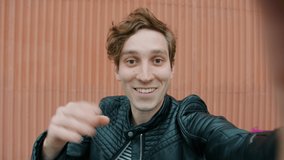 POV portrait of cheerful young guy making video call waving hand and speaking standing outdoors alone enjoying friendly communication. People and technology concept.