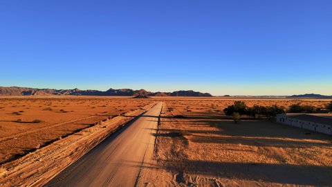 Drone shot of empty road in national park in africa. Natural landscape with highway in a middle of golden desert under clear blue sky. Barren wilderness of sand plain captured by drone.