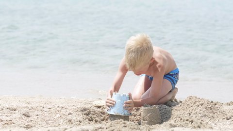Little blonde boy playing with sand on beach ocean sea. Child building sand castle house. Family summer holidays and trips to warm countries