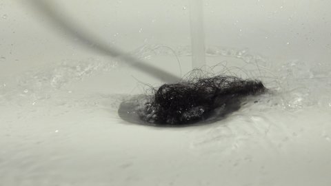 A piece of hair is moved by a stream of water and falls into the drain pipe of the bathtub. The concept of health problems.