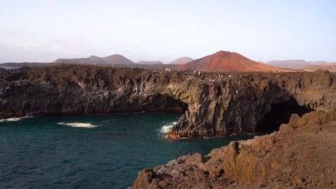 Lanzarote island, caves in Los Hervideros tourist attraction with red mountain on background in Lanzarote. Volcanic coast landmark on sunny day in Canary Islands