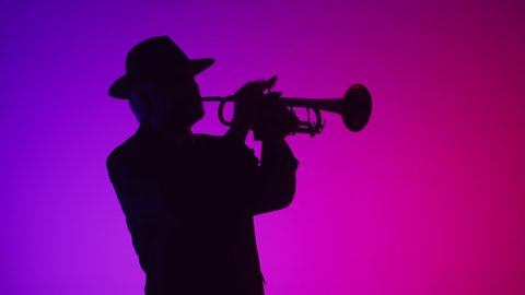 Silhouette of man in hat, playing musical trumpet and dancing. Studio, neon. Concept of jazz music, art and talent