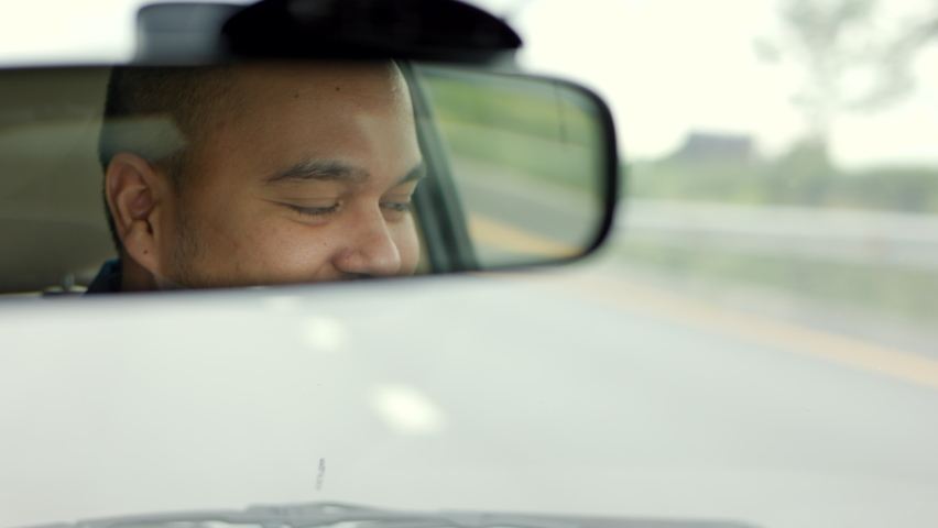 Rear view mirror. Close up shot eye of young asian man looking roadway while driving car in the morning. Man sitting in car. | Shutterstock HD Video #1077940349