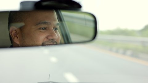 Rear view mirror. Close up shot eye of young asian man looking roadway while driving car in the morning. Man sitting in car.
