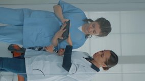 Vertical video: Professional dentist talking to nurse and looking at digital tablet for teeth diagnosis after examination in dental cabinet. Orthodontical team using device tool for dentistry