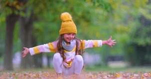 Little girl in autumn park laughing and playing with fallen colorful leaves. Fall season.
