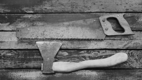 Close-up top view black and white flatlay 4k video of old used vintage tools. Man puts on and takes off old rusty saw and axe from weathered wooden surface background