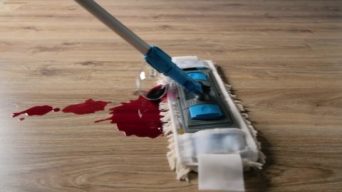 Spilled wine on the laminate floor is cleaned with a mop close-up.