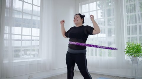 Fat Asian woman playing hula hoop to lose weight cheerfully in her room. health and weight loss concept
