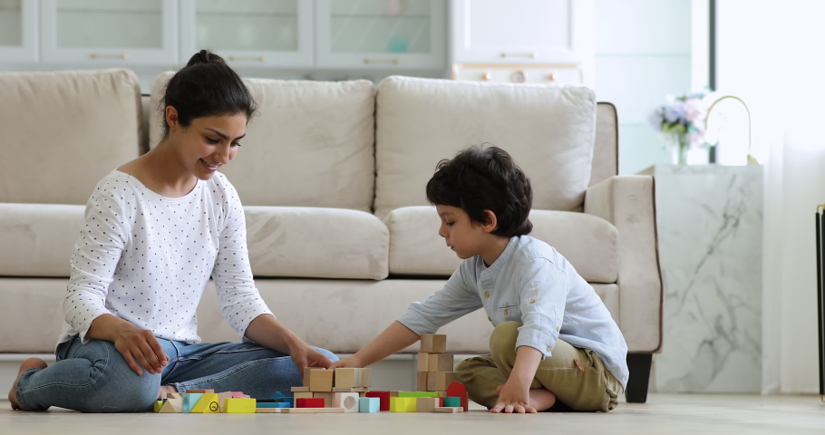 Young Indian woman and little preschooler cute son play colorful wooden bricks sit on warm floor in modern living room. Children development, babysitting job, leisure games on weekend at home concept Royalty-Free Stock Footage #1077958223