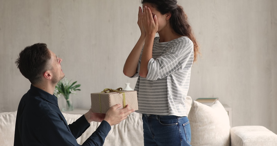 Amazed young woman opening eyes, getting gift from beloved man. Loving attentive millennial husband presenting wrapped box to beautiful excited wife, congratulating with birthday or anniversary. Royalty-Free Stock Footage #1077958307