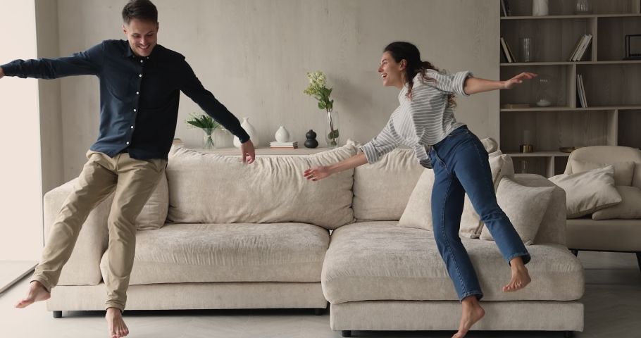 Overjoyed happy sincere young couple homeowners or renters jumping on big comfortable sofa, enjoying moving into new contemporary apartments, real estate service, bank mortgage loan, tenancy concept. | Shutterstock HD Video #1077958313