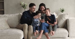 Joyful sincere young couple parents using cellphone with little children siblings, playing mobile games, recording funny video for social network, shopping in internet store, entertaining online.