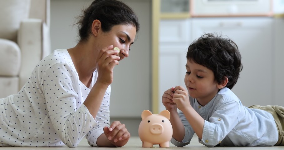 Young Indian mother her little 4s son lying on floor at home count and drop coins into piggy bank. Caring parent teaches child save money, think about future, manage personal finances, savings concept | Shutterstock HD Video #1077958364