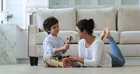 Indian woman play with cute 4s son settled down on warm floor in living room repairing toy truck using screw driver, having fun together at home. Help and support, leisure game with children concept