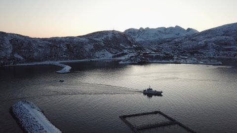 Dlog flat Aerial Drone view Norway Fishing Boat entering the snowy and icy harbour with mountains and coastline in the background in winter