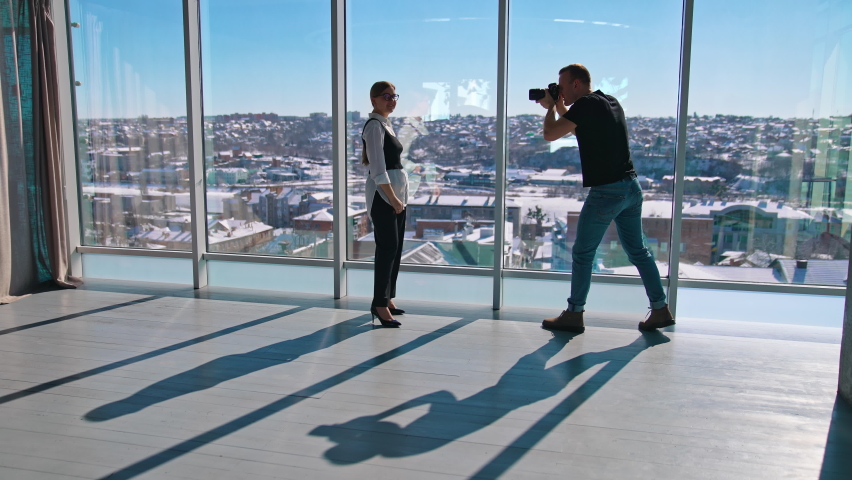 Business woman posing on camera near office window. Young photographer taking photos of a beautiful woman in business clothes on the background of windows.