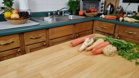 Home cooking - Panning left to right of vegetables like carrot, rooted parsley, celery and parsnip being ready on kitchen table to be cleaned for cooking.