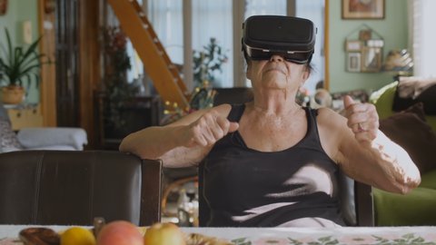 90 year old woman playing video game uses vr headset. She is having fun while playing with a virtual reality headset.