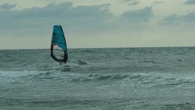 A person rides on a board with a sail, windsurfing. Summer entertainment is an extreme sport. Water sports, windsurfing, sailing. Storm. Slow-motion video.