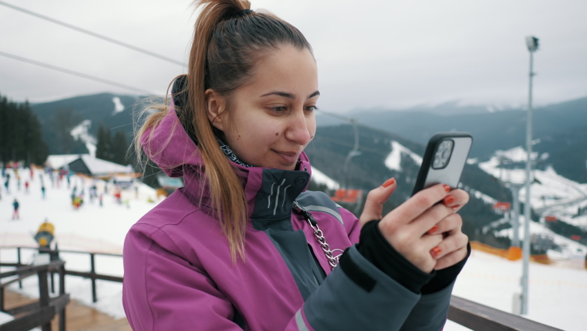 Close-up portrait of young beautiful woman uses a mobile phone on the lift of a ski resort, mountains and skiers in the background Royalty-Free Stock Footage #1077968036