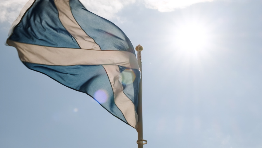 Slow motion view of the flag of Scotland, also known as St Andrews Cross, flying against a bright blue sky Royalty-Free Stock Footage #1077969260