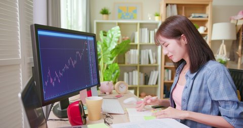 asian woman has stock market or cryptocurrency investment from home by computer and she is looking at chart