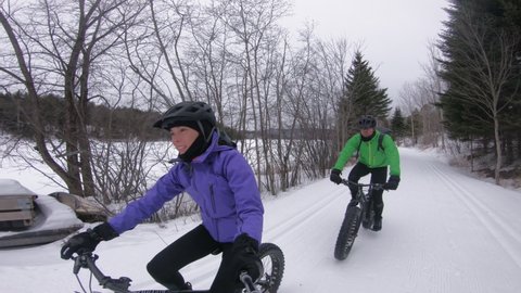 Fatbike in winter forest. Fat biking people riding bicycle in the snow in winter. Selfie video by woman and man living healthy outdoor active winter sports lifestyle