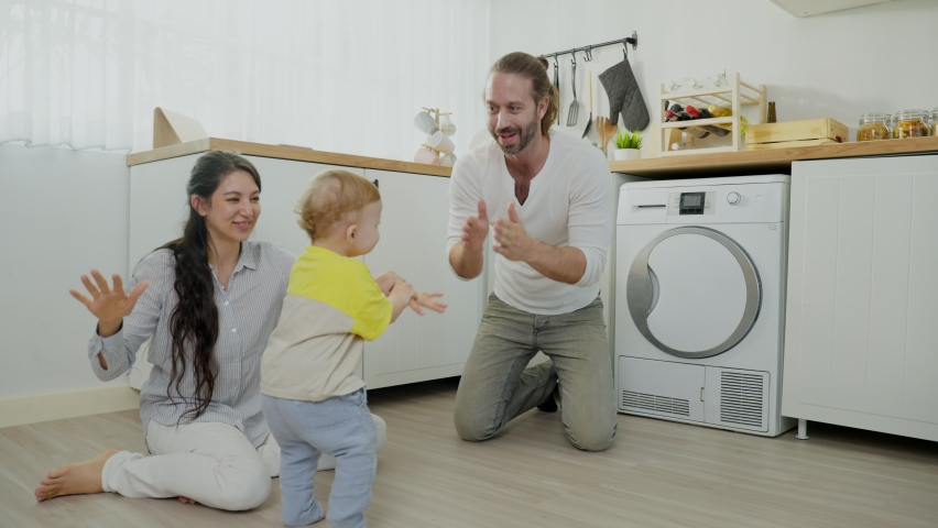 Caucasian loving parent play with baby boy child on floor in kitchen. Happy family, attractive beautiful young couple dad and mom dance with cute infant toddler son enjoy activity relationship at home
