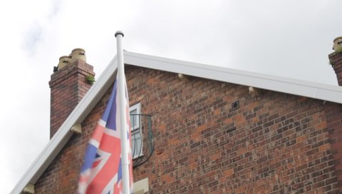 Union Jack flag blowing in the wind against gable end of a house 