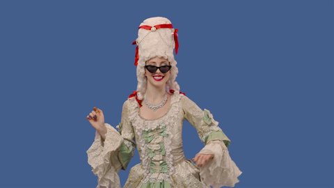 Portrait of courtier lady in white vintage lace dress, wig and sunglasses smiles coquettishly and flirts. Young woman posing in studio with blue screen background. Close up. Slow motion ready 59.94fps
